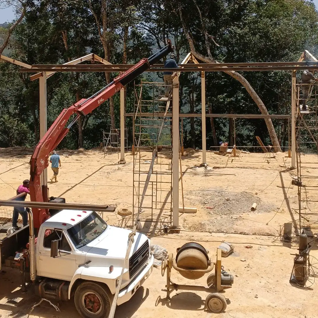 Grúa camión izando una viga metálica en el montaje de una estructura entre árboles