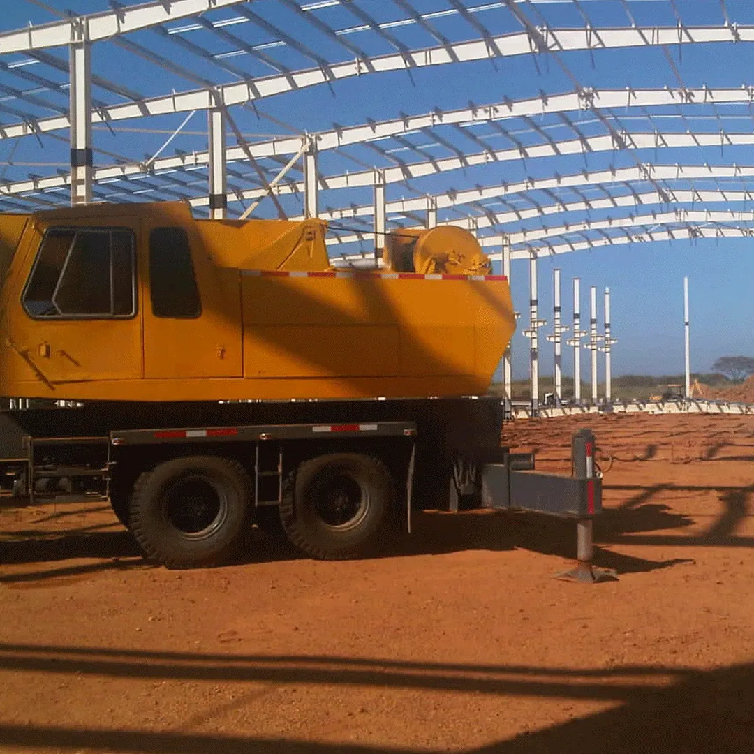 Grúa móvil amarilla bajo la estructura metálica de un galpón
