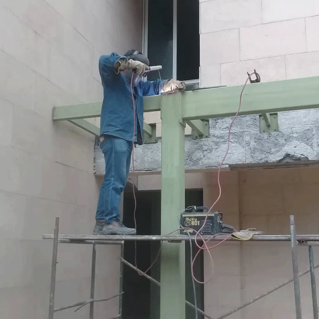 Soldador en andamio trabajando sobre la columna de una fachada